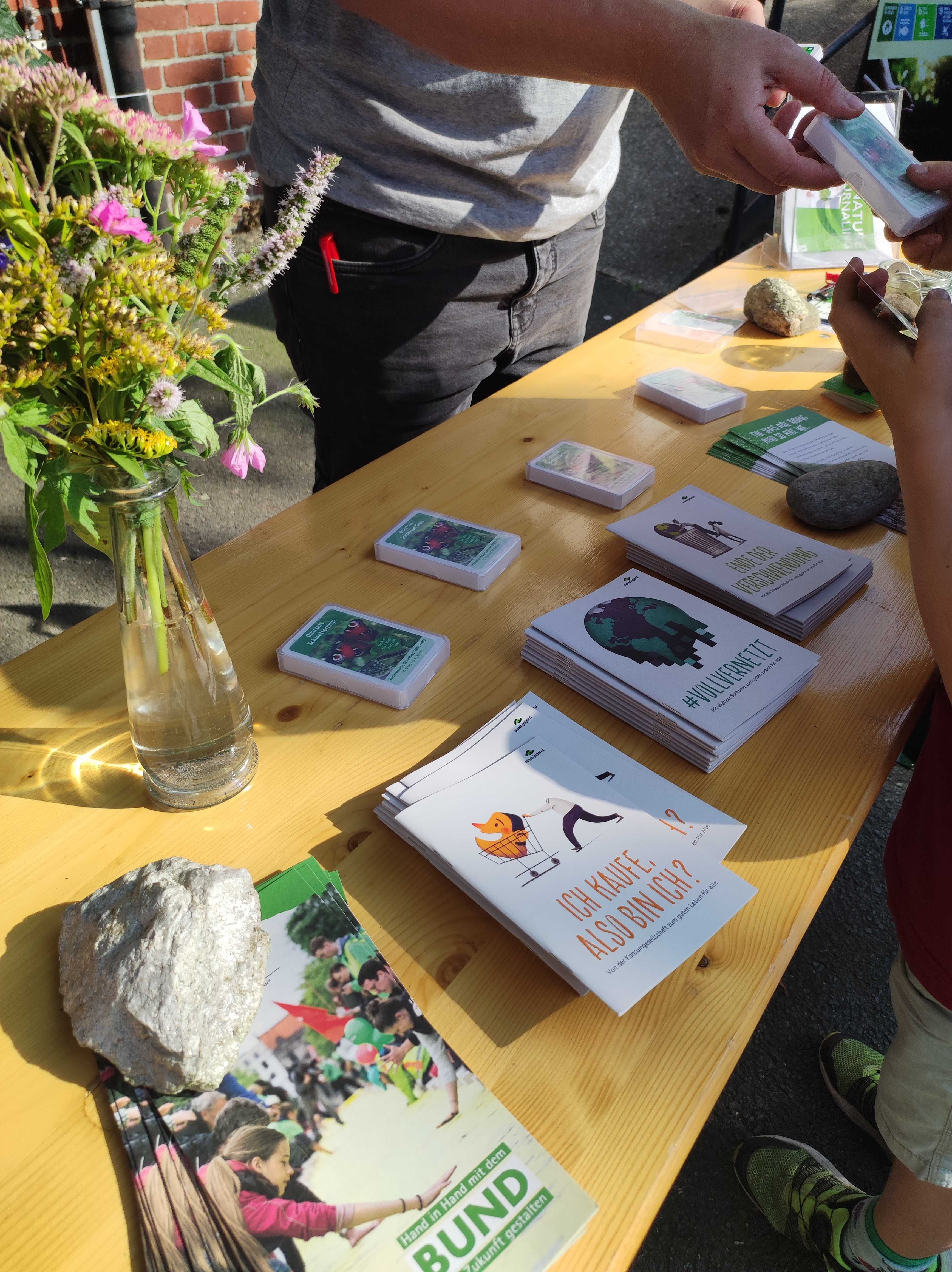 Infostand mit Broschüren und Blumen auf Holztisch.