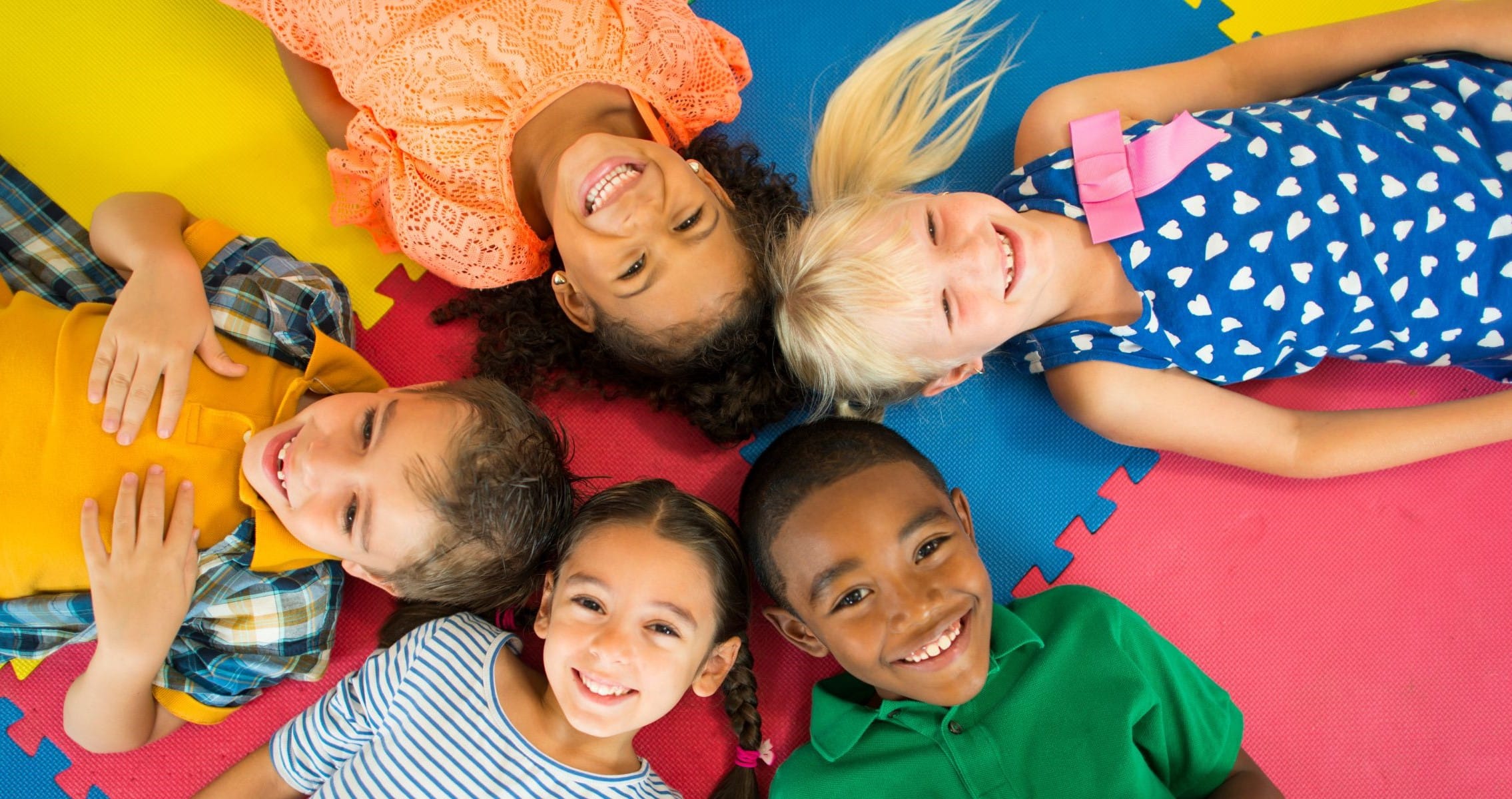 Lachende Kinder liegen auf bunten Matten