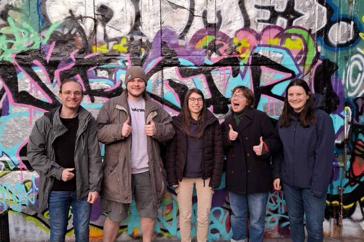 Fünf Personen vor Graffiti-Wand stehend, Daumen hoch.